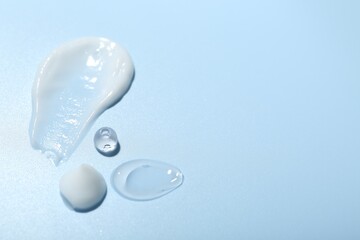 Cream and gel samples on light blue background, closeup. Space for text