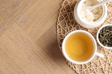 Refreshing green tea in cup, sugar bowl and dry leaves on wooden table, top view. Space for text