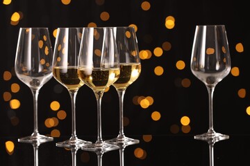 Tasty white wine in glasses on mirror surface against dark background with blurred lights. Bokeh effect