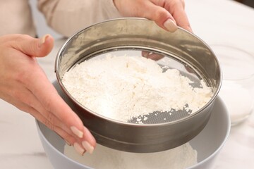Making dough. Woman sifting flour into bowl at white table, closeup