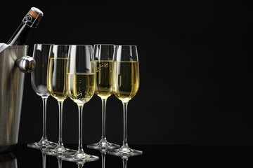 Bottle of sparkling wine in cooler bucket and glasses on black mirror surface. Space for text