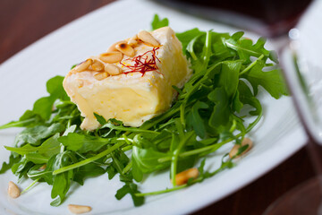 Soft cheese camembert served with pine nuts and arugula on white plate