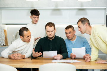 Fototapeta premium Brainstorming - male friends trying to solve financial problems by consulting at the table in the home kitchen