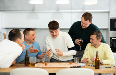 Friends drinking beer and enthusiastically playing a board game at home