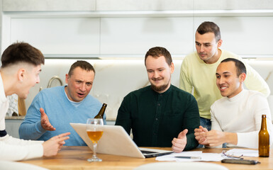 Group of football fans drinking beer and watching football match on a laptop at home