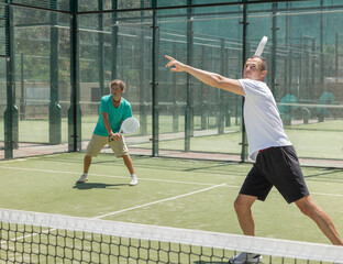 Four men practice playing padel on an outdoor tennis court