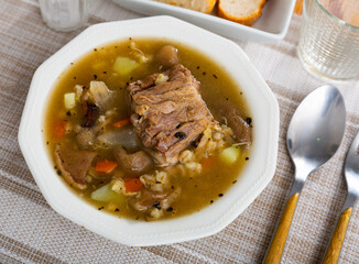 Hearty homemade soup with forest mushroom, pork, vegetables and pearl barley. Russian cuisine..