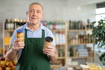 Polite mature male seller holding some jars of beans in grocery store