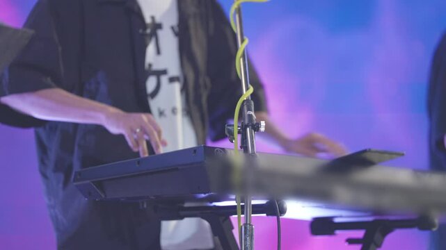 A man is playing a keyboard with a microphone in front of him. The keyboard is black and the microphone is yellow. The man is wearing a black shirt