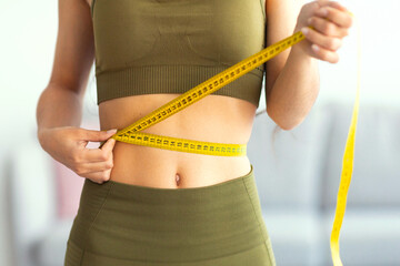 Cropped view of slim Indian woman measuring her waist with tape measure at home, closeup....