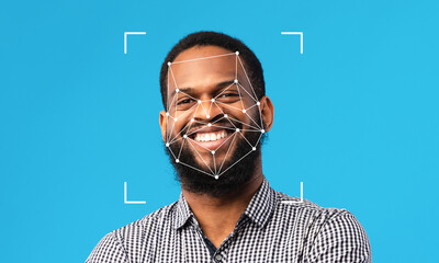 A man smiles confidently against a blue background as facial recognition technology analyzes his features. This highlights advancements in identification processes and their growing presence.