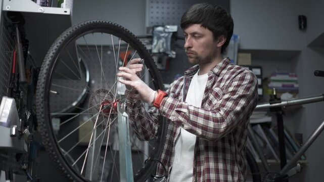 Working alignment of rim and spokes of bicycle wheel on wheel stand in bike repair shop. Bike repairman with specialized tool in workshop tightening wheel spokes. Cycle mechanic fixes wheel. 