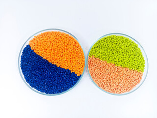 Red, blue masterbatch granules in glass cup, polymer carrying pigment with chips poured in white...