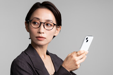 ジャケットを着て眼鏡をかけた女性がスマートフォンを手に持っている。