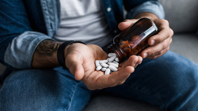 Man pouring capsules from bottle, hold pills on hand. Overdose of medication and pain. Depressed sad unhappy millennial caucasian guy wants to die, commit suicide, cropped, close up, , empty space