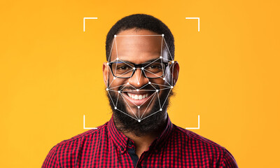 A smiling person with glasses poses against a bright yellow backdrop, featuring facial recognition markers superimposed on their face, illustrating identification technology in action.
