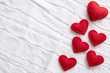 Fototapeta premium White textured background with several red heart-shaped objects made of felt arranged.