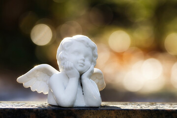 a small white angel figure on a gravestone looks longingly towards the sky against a blurred background with bokeh bubbles