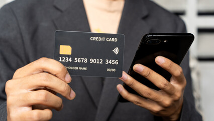 Hand holding black credit card while holding a handphone