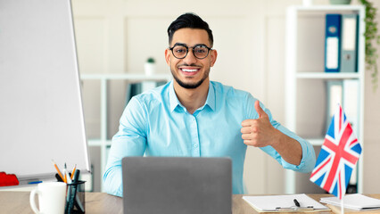 Young Arab tutor conducting online English lesson, showing thumb up, teaching foreign language from...