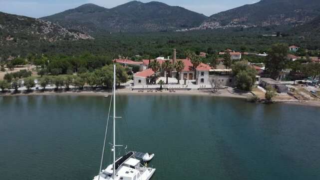 A luxury yacht sailing at seaport with Zaira hotel estate in background surrounded with olive trees garden landscape and mountains, Mytilene, Lesvos Island, Aerial view