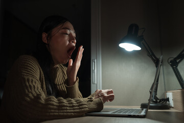 sleepy woman yawning while working with laptop at night