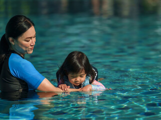 mother teaching toddler baby girl swimming in pool and wearing life jacket