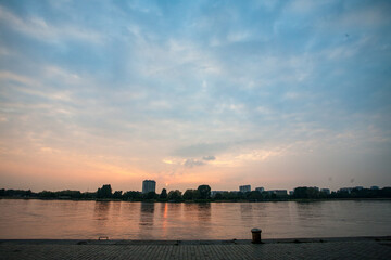 Fototapeta premium A beautifully serene river sunset with soft clouds that perfectly reflects a stunning city skyline on the water