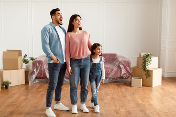 Moving And Choosing New Home. Full Body Length Of Happy Excited Family Standing In Living Room In...