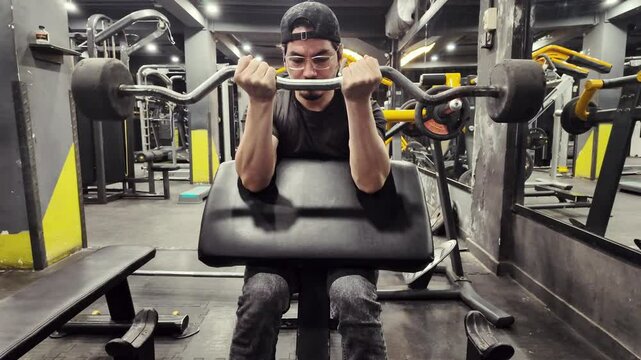 Closeup View of a Young Man Training Biceps with EZ Bar Preacher Curls in an Empty Gym