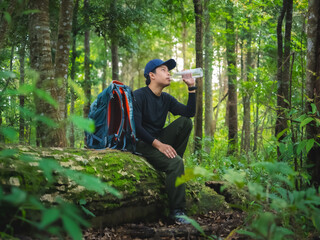 Solo hiker takes break to drink water while sitting on fallen tree in lush rainforest at Phu Soi Dao National Park, Thailand.