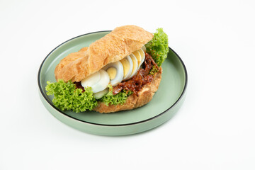 The perfect on-the-go breakfast or lunch: a delicious croissant sandwich on a round plate isolated on white background