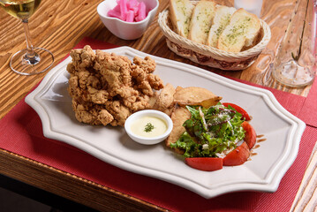 Fried chicken pieces, wedge fries, and tomato salad on a white plate
