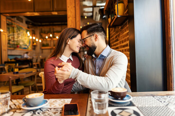Romantic affectionate couple hugging, cuddling and holding hands in cafeteria on their date.