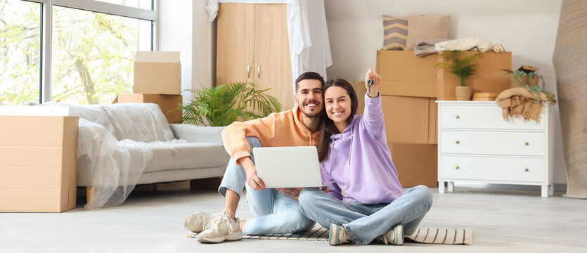 Young couple with keys and laptop sitting in room on moving day