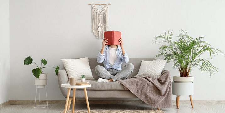 Pretty young woman reading book on sofa near white wall