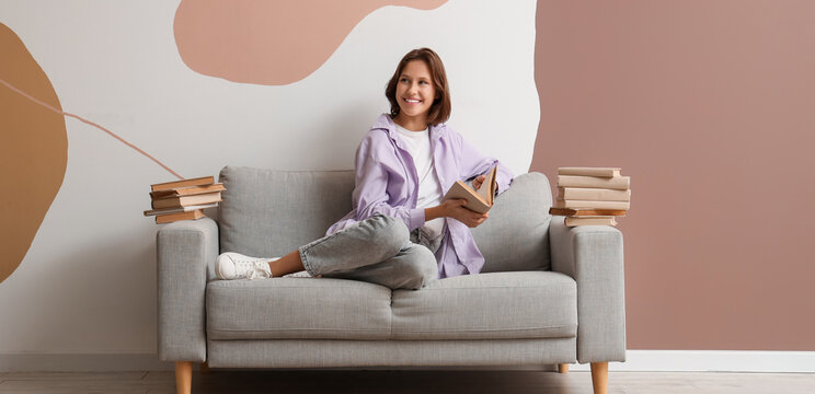 Pretty young woman reading book on sofa at home