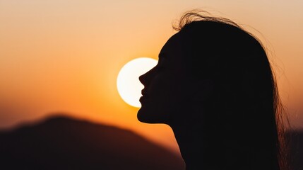 Fototapeta premium woman stands in profile as she enjoys a breathtaking sunset. warm orange glow of the sun casts a beautiful shadow, highlighting the contours of her face against the landscape