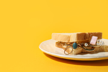 Plate with bread slices and jewelry on yellow background