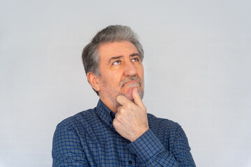 Senior man thinking with a gesture of doubts and looking up, photo with copyspace.