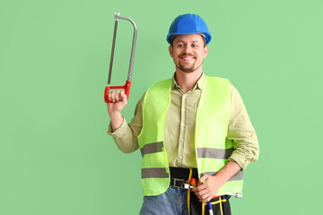 Male builder with hacksaw on green background