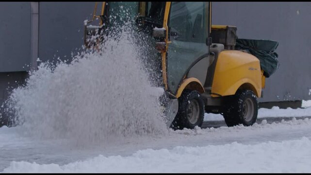 A yellow snow-clearing vehicle sprays a powerful wave of snow, showcasing efficient winter road maintenance. The snowy environment and dynamic action highlight urban winter solutions in motion.