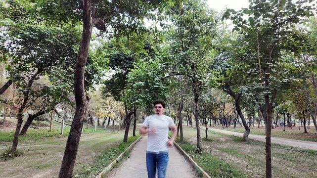 Young Man Running on a Track in the Park, with Trees, Evening Light, and Cars in the Background, Highlighting Cardio and Heart Rate Exercise