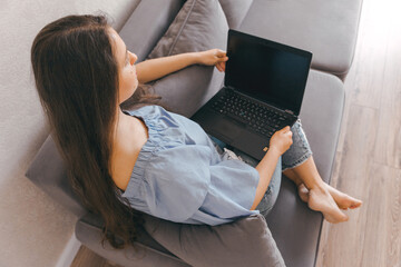 Naklejka premium A young beautiful girl is sitting on the couch with a laptop. Top view