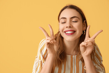 Pretty young woman showing peace gestures on orange background