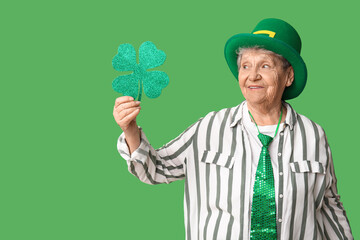 Senior woman in leprechaun hat with clover on green background. St. Patrick's Day celebration