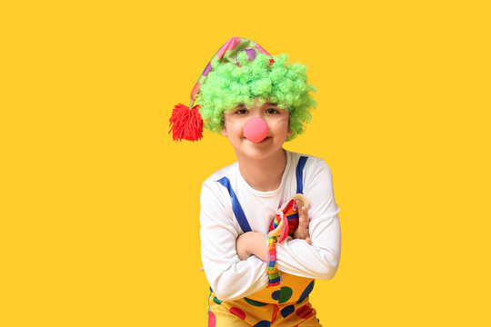 Funny little boy in clown costume cross hands on yellow background. April Fools Day celebration