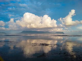 Obraz premium Idyllic sand beach and low tide sea reflecting dramatic sky with fluffy clouds in Bako National Park, Kuching, Sarawak, Malaysia. Calm water with mirror-like effect on Borneo island. Magical spectacle