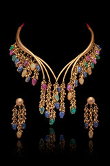 A beautiful golden Necklace and Earrings with green emerald stones, ruby, and diamonds, on a black background.