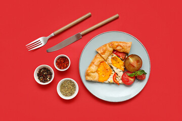 Plate with pieces of tasty tomato galette and spices on red background